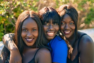Three african american friends smiling happy sitting on the bench at the park.