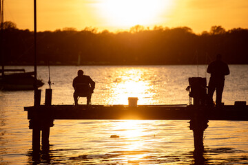 Silhouette of people fishing off of a dock or pier during sunset golden hour or sunrise