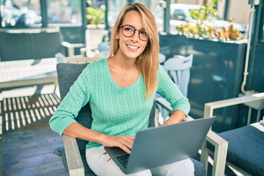 Young blonde woman smiling happy working using laptop sitting at the coffee shop terrace.