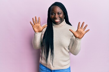 Young black woman with braids wearing casual winter sweater showing and pointing up with fingers number ten while smiling confident and happy.