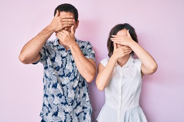 Beautiful couple wearing casual clothes covering eyes and mouth with hands, surprised and shocked. hiding emotion