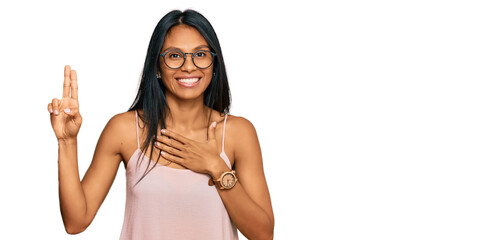 Young african american woman wearing casual clothes and glasses smiling swearing with hand on chest...