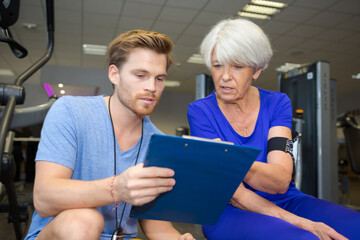 personal trainer holding clipboard with senior woman in fitness centre