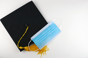 Graduation cap and medical mask on a white background, copy space. The concept of college and university graduates during a pandemic. Protection from the virus while studying.