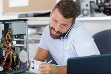Fototapeta na wymiar young male contractor repairing computer having phone call