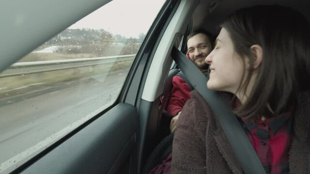 Loving couple, man and woman sitting on a passenger seats of the car driving at the highway, woman sends air kiss to a man