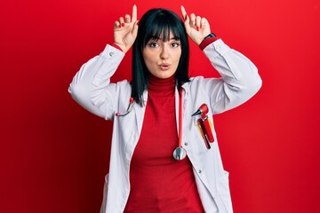 Young hispanic woman wearing doctor uniform and stethoscope doing funny gesture with finger over...