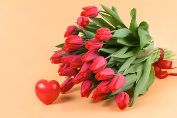 A large bouquet of red tulips and heart lie on a soft beige background - spring flowers for the holiday of March 8 or Valentines Day. With love and tenderness. A postcard