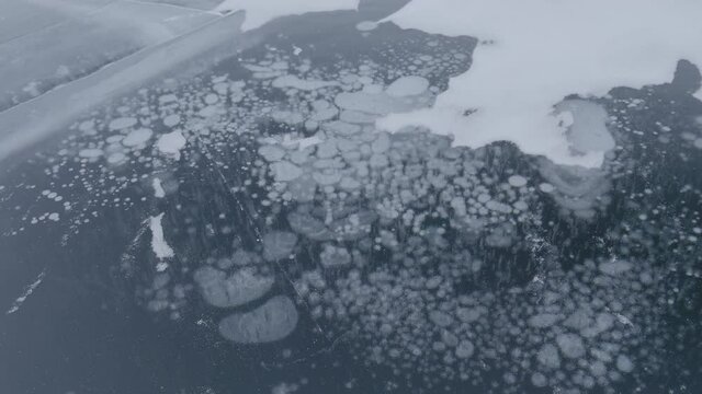 Methane bubbles frozen in Arctic lake surface ice - Climate change raises methane CH4 gas under an Arctic circle lake's solid surface. Permafrost is a climate emergency tipping point. Ungraded V-LOG