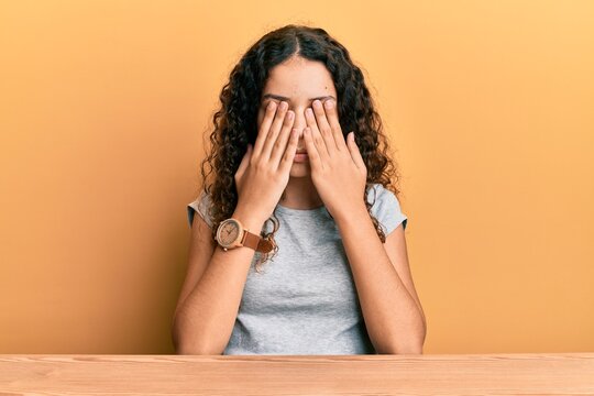 Teenager hispanic girl wearing casual clothes sitting on the table rubbing eyes for fatigue and headache, sleepy and tired expression. vision problem