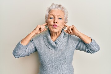 Senior grey-haired woman covering ears with finger looking at the camera blowing a kiss being lovely and sexy. love expression.