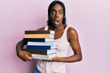 Young african american woman holding books afraid and shocked with surprise and amazed expression, fear and excited face.