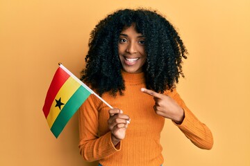 African american woman with afro hair holding ghana flag smiling happy pointing with hand and finger