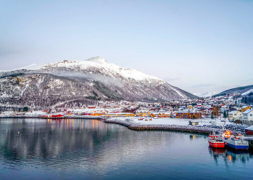 Norway, the village Ornes in December. Typical wooden houses on the coastline and in the background snow covered mountains.