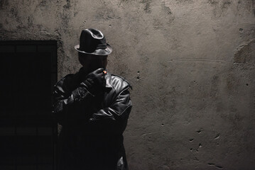Detective spy agent is smoking a cigarette on a concrete wall background.