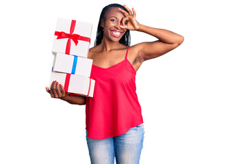 Young african american woman holding gift smiling happy doing ok sign with hand on eye looking through fingers