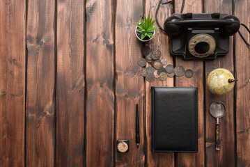 Old coins, black rotary phone, leather book, magnifying glass, inkwell and quill pen on the brown wooden desk background with copy space.