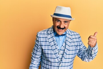 Mature middle east man with mustache wearing vintage and elegant fashion style smiling with happy face looking and pointing to the side with thumb up.