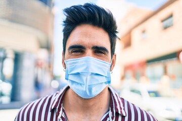 Young handsome hispanic man with beard outdoors wearing coronavirus safety mask