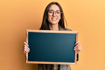 Young hispanic girl holding blackboard smiling with a happy and cool smile on face. showing teeth.
