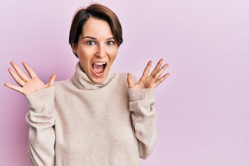 Young brunette woman with short hair wearing casual winter sweater celebrating crazy and amazed for success with arms raised and open eyes screaming excited. winner concept