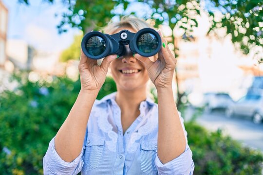 Young blonde woman smiling happy looking for new opportunity using binoculars at the park,