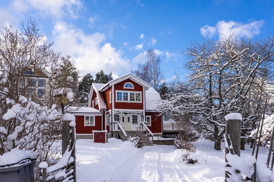 Traditional old big red wooden houses in winter countryside. Old wooden fence covered with snow in the foreground. Entrance gates to the courtyard. Beautiful red cottages or villas. 
