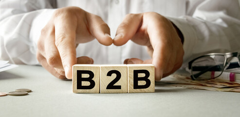 B2B inscription on the texture of wooden cubes. A business man holds a cube in his hand. An inscription on a financial, business or economic theme.