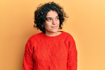 Young hispanic woman with curly hair wearing casual winter sweater smiling looking to the side and staring away thinking.