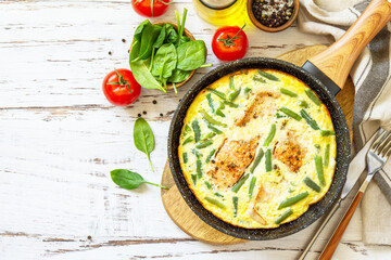 Healthy breakfast or diet lunch. Rustic omelet (omelette, Scrambled)  with salmon fillet and green beans in a frying pan on a white kitchen wooden table. Top view flat lay. Copy space.