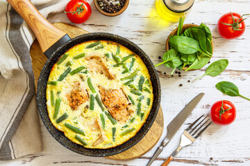 Healthy breakfast or diet lunch. Rustic omelet (omelette, Scrambled)  with salmon fillet and green beans in a frying pan on a white kitchen wooden table. Top view flat lay.