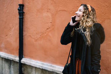 Young blonde woman making a cell phone call on the street on an orange wall.