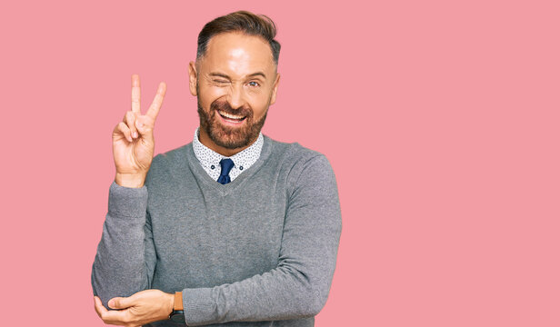Handsome middle age man wearing business clothes smiling with happy face winking at the camera doing victory sign with fingers. number two.