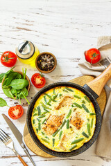 Healthy breakfast or diet lunch. Rustic omelet (omelette, Scrambled)  with salmon fillet and green beans in a frying pan on a white kitchen wooden table. Top view flat lay. Copy space.