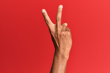 Hand of hispanic man over red isolated background counting number 2 showing two fingers, gesturing victory and winner symbol