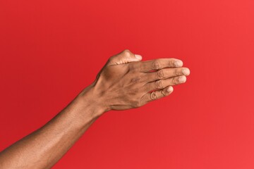 Hand of hispanic man over red isolated background stretching and reaching with open hand for handshake, showing back of the hand