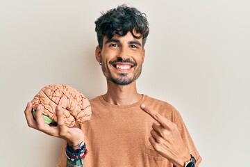 Young hispanic man holding brain smiling happy pointing with hand and finger