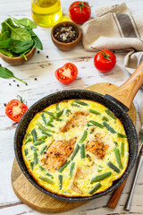 Healthy breakfast or diet lunch. Rustic omelet (omelette, Scrambled)  with salmon fillet and green beans in a frying pan on a white kitchen wooden table.