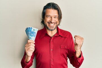 Middle age handsome man holding 50 polish zloty banknotes screaming proud, celebrating victory and...