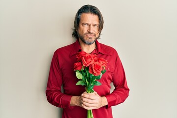 Middle age handsome man holding bouquet of red roses skeptic and nervous, frowning upset because of problem. negative person.