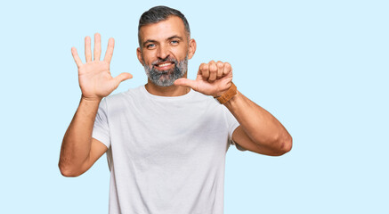 Fototapeta premium Middle age handsome man wearing casual white tshirt showing and pointing up with fingers number six while smiling confident and happy.