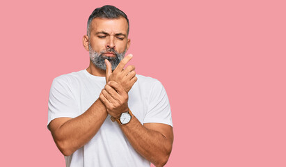 Middle age handsome man wearing casual white tshirt suffering pain on hands and fingers, arthritis...
