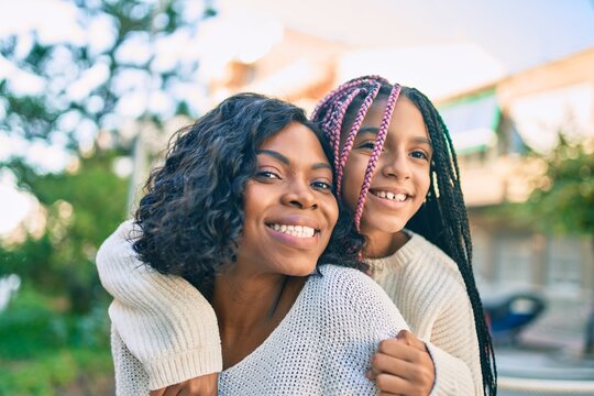 Beautiful african american mother giving daughter piggyback ride smiling happy at the park.