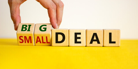 Big or small deal symbol. Businessman turns a wooden cube and changes words 'small deal' to 'big deal'. Beautiful yellow table, white background, copy space. Business and big or small deal concept.