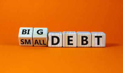 Big or small debt symbol. Turned wooden cubes and changed words 'small debt' to 'big debt'. Beautiful orange table, orange background, copy space. Business and big or small debt concept.