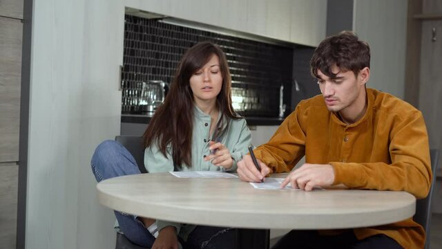 A young couple of spouses is sitting at a table in the kitchen and calculating the expenses and income of the family. Record keeping to maintain financial stability.