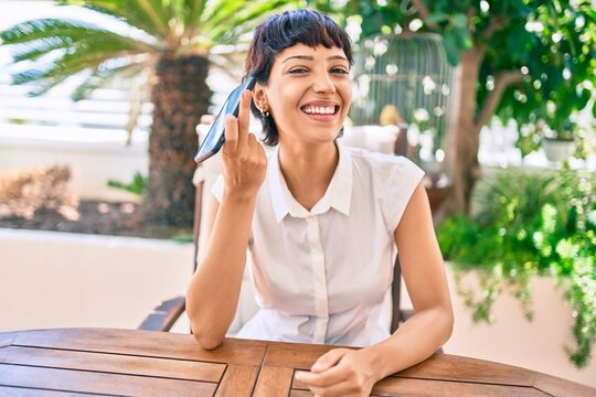 Beautiful woman with short hair sitting at the terrace on a sunny day listening to voice message on the phone