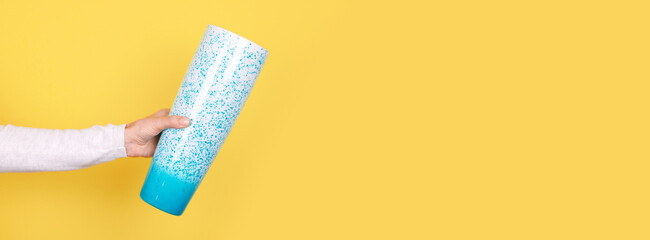 Hand with turquoise glass vase on yellow background.