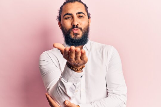 Young arab man wearing casual clothes looking at the camera blowing a kiss with hand on air being lovely and sexy. love expression.
