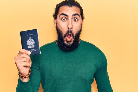 Young arab man holding canada passport scared and amazed with open mouth for surprise, disbelief face